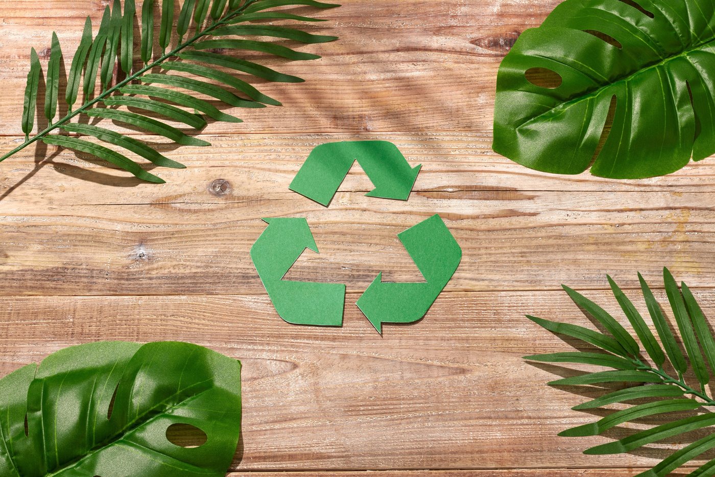 Símbolo de reciclaje sobre madera con hojas verdes